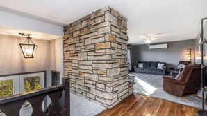 A living room with a stone fireplace, a wooden floor, a grey sofa, and a brown armchair.