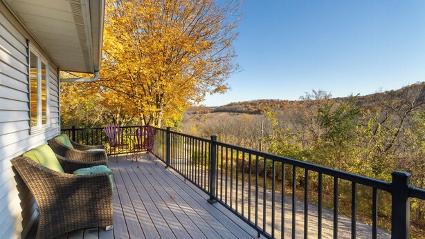 A wooden deck with wicker furniture and a black railing overlooking a forested area.