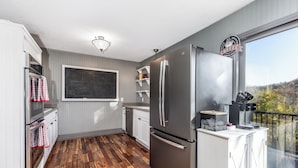 A kitchen with wooden flooring, white cabinetry, a stainless steel refrigerator, and a chalkboard wall.