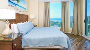 Een hotelkamer met een bed, twee bedlampen, een nachtkastje, een plafondventilator en een groot raam met gordijnen.