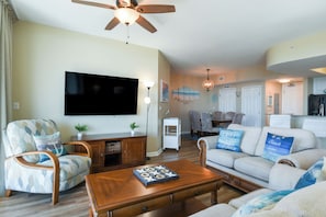 A living room with a flat-screen TV, wooden furniture, and a ceiling fan.