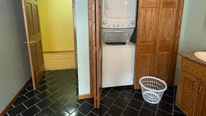 A laundry room with a washing machine and dryer, a white laundry basket, and wooden cabinets. - Spacious 4-bedroom at La Casa della Nonnina (Negaunee)