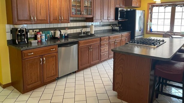A kitchen with wooden cabinets, a stainless steel dishwasher, a gas stove, and a large island with bar stools. - Spacious 4-bedroom at La Casa della Nonnina (Negaunee)