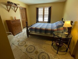 Un dormitorio con cama, cómoda, ventana y lámpara.