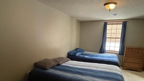 A bedroom with two beds, a small round table, a dresser, and a window with curtains. - Spacious 4-bedroom at La Casa della Nonnina (Negaunee)