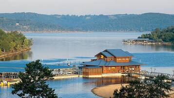 A lakeside lodge with a large wooden building, docked boats, and a view of the lake and hills.