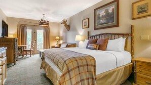 A hotel room with a large bed, a wooden headboard, a desk, and a chair. There is a chandelier, a deer head decoration, and framed pictures on the wall. - Family Fun at Wilderness Club at Big Cedar! (Ridgedale)