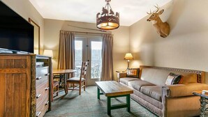 A hotel room with a wooden dresser, a television, a dining table with chairs, a sofa, a mounted deer head, and a chandelier. - Family Fun at Wilderness Club at Big Cedar! (Ridgedale)