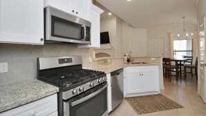 Una cocina moderna con armarios blancos, electrodomésticos de acero inoxidable, encimeras de granito y un comedor con candelabro.