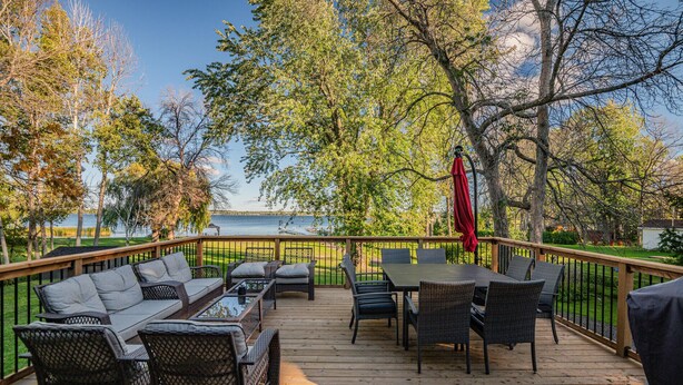 Um deck de madeira com móveis de exterior, incluindo um sofá, cadeiras e uma mesa, com vista para um lago.