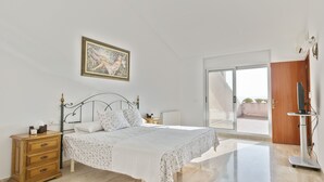 A bedroom with a bed, a dresser, a painting, and a sliding glass door leading to a balcony.