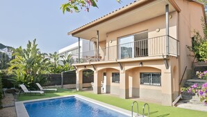 A two-story house with a swimming pool, a balcony, and a garden with tropical plants.