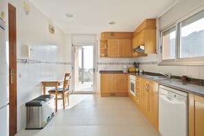 A kitchen with wooden cabinets, a Bosch dishwasher, a sink, and a dining area with a chair and table.