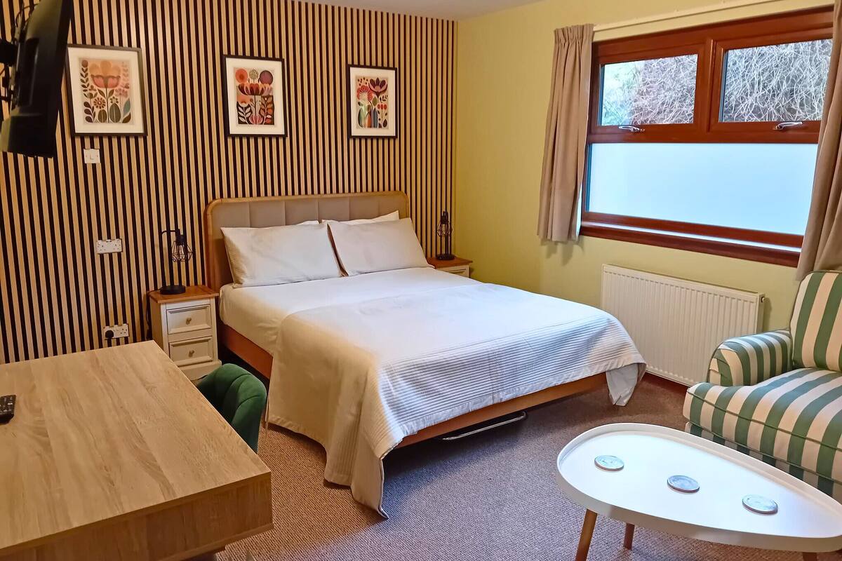 Une chambre d’hôtel avec un lit, une table de chevet, une chaise et une fenêtre avec des rideaux.