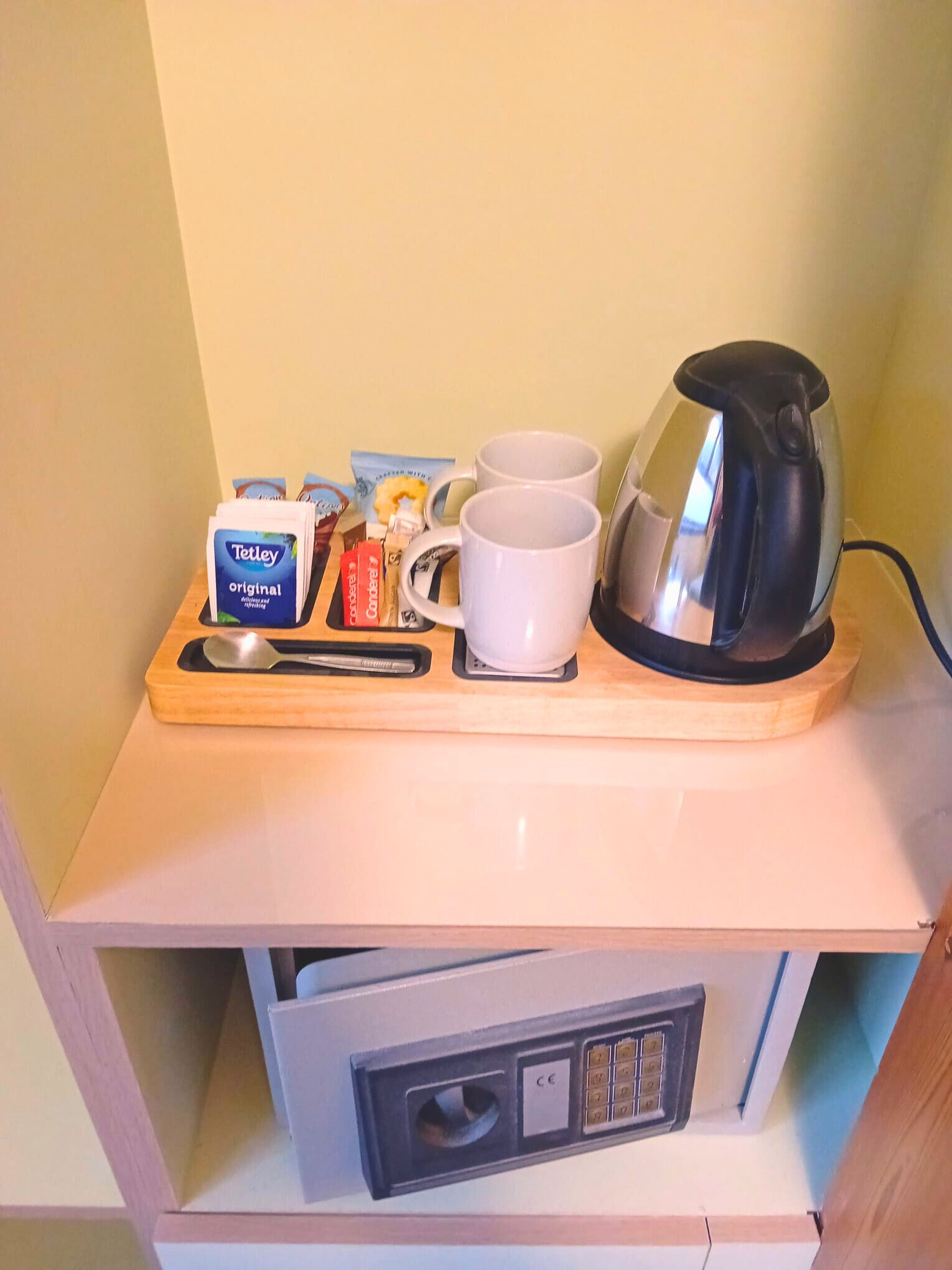 Un plateau de petit-déjeuner avec une bouilloire, deux tasses, une cuillère et quelques condiments, posé sur une table en bois.