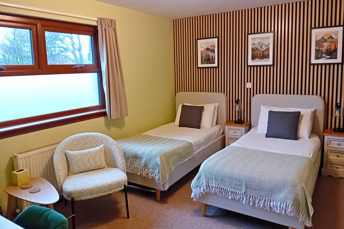 Une chambre avec deux lits simples, une chaise, une petite table et un radiateur.