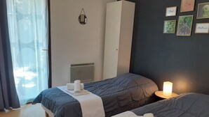 A hotel room with two beds, a wardrobe, a heater, and framed pictures on the wall.
