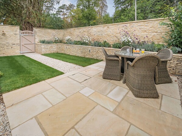 A patio area with stone flooring, a grassy lawn, wicker furniture, and a stone wall.