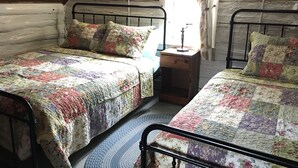 A cozy attic bedroom with two metal beds, a small wooden nightstand, and a wall-mounted light fixture. - "Little House on the Prairie" with modern plumbing! (Coon Valley)