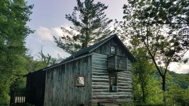 A rustic log cabin with a balcony, surrounded by lush greenery and trees. - "Little House on the Prairie" with modern plumbing! (Coon Valley)