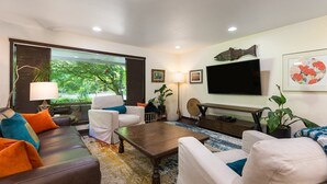 A modern living room with a sofa, armchairs, a coffee table, and a TV. There are plants, artwork, and a large window with a view of greenery. - Well-furnished Hiker's Retreat, Centrally located for visiting the ONP; Sleeps 8 (Port Angeles)