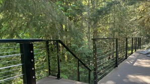 A wooden pedestrian bridge with metal railings, surrounded by dense green foliage. - Well-furnished Hiker's Retreat, Centrally located for visiting the ONP; Sleeps 8 (Port Angeles)