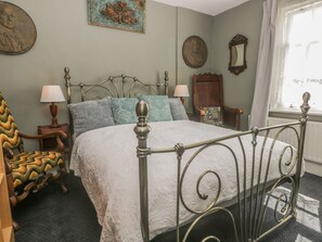 A bedroom with a metal bed frame, a wooden chair with a patterned cushion, a nightstand with a lamp, and a window with curtains. - Highview (Scarborough)