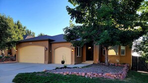 A two-story house with two garage doors, a landscaped front yard with a stone border, and a tree providing shade. - 5 Bedroom home near downtown with hot tub! (Colorado Springs)