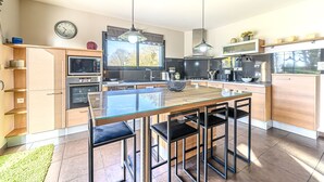 Una cocina moderna con una mesa de comedor de vidrio, taburetes negros, electrodomésticos de acero inoxidable e iluminación colgante.