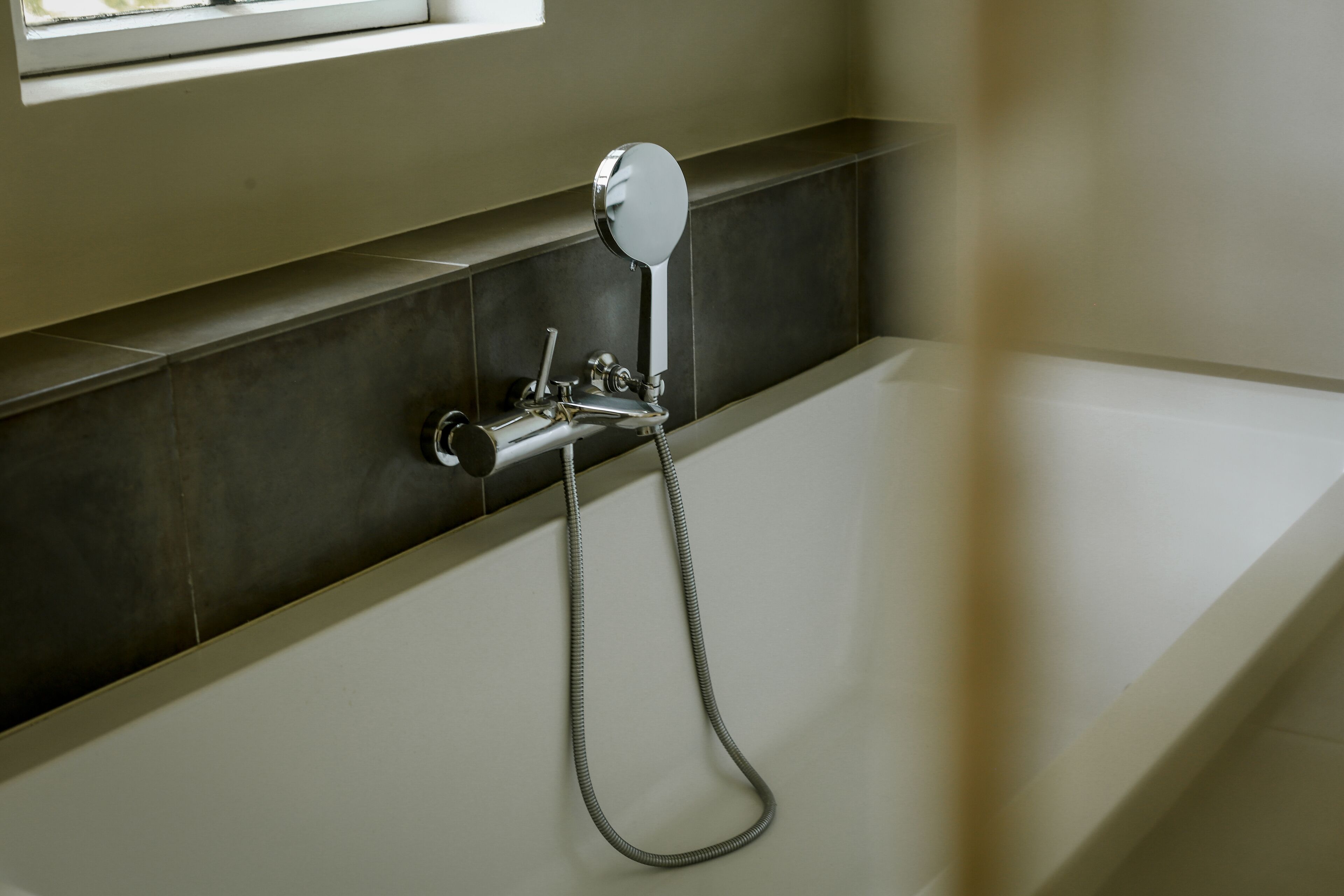 A modern bathroom with a bathtub, a handheld showerhead, and a wall-mounted mirror.