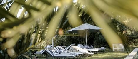A poolside area with lounge chairs and umbrellas, surrounded by greenery.