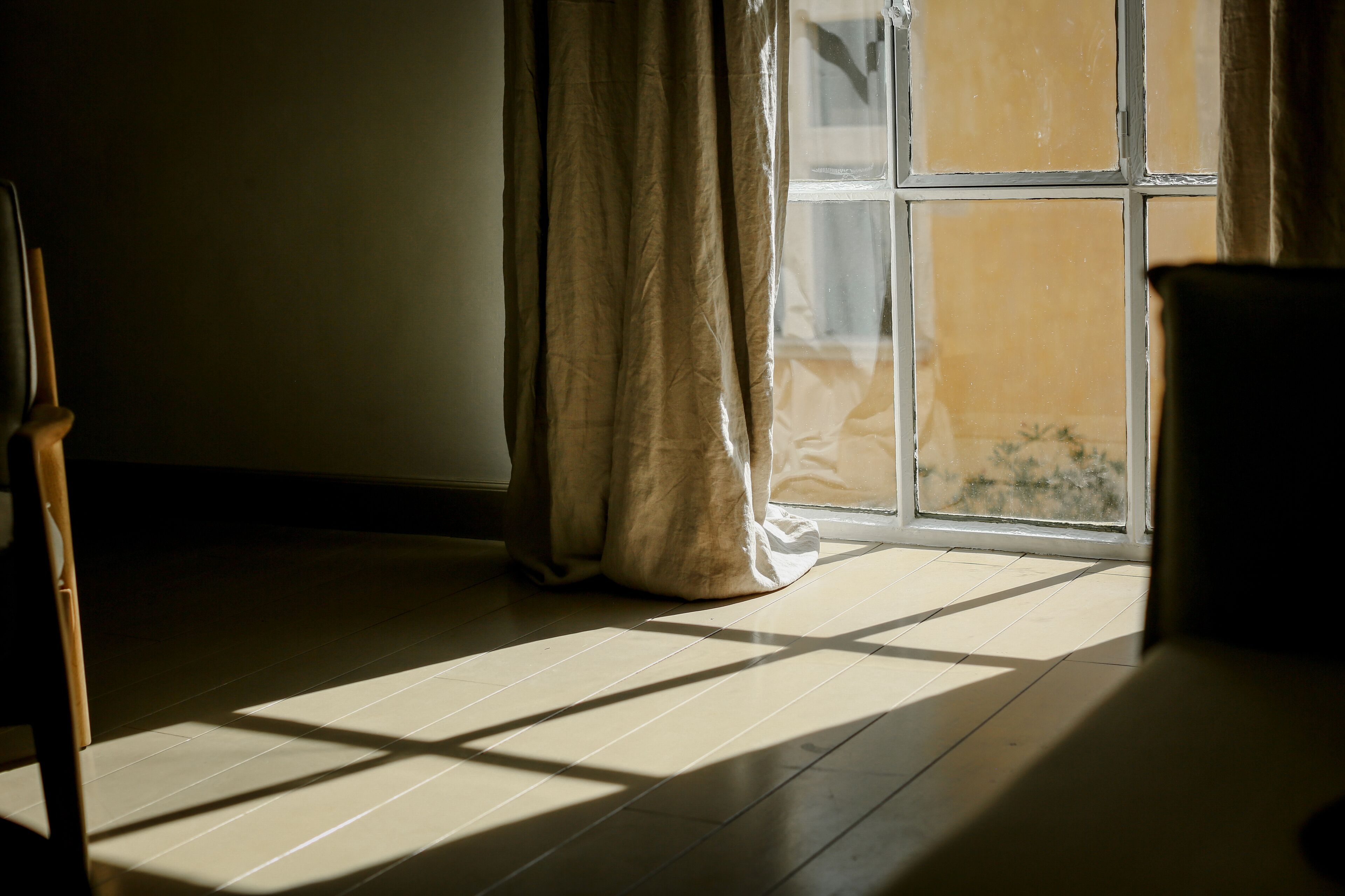 A room with a large window, wooden floor, and a curtain partially drawn.