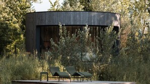 Een modern gebouw met een ronde structuur en een terras met lounge fauteuils.
