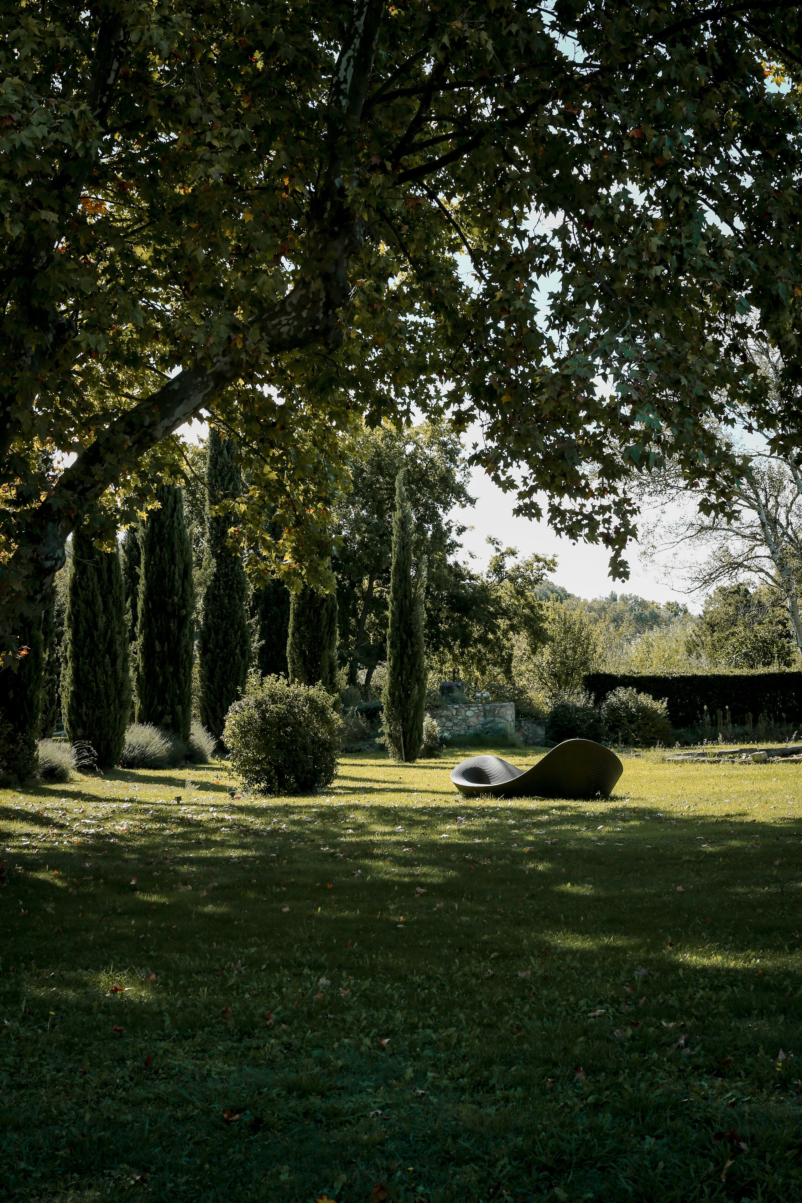 A serene outdoor area with a grassy lawn, a curved bench, and tall trees providing shade.