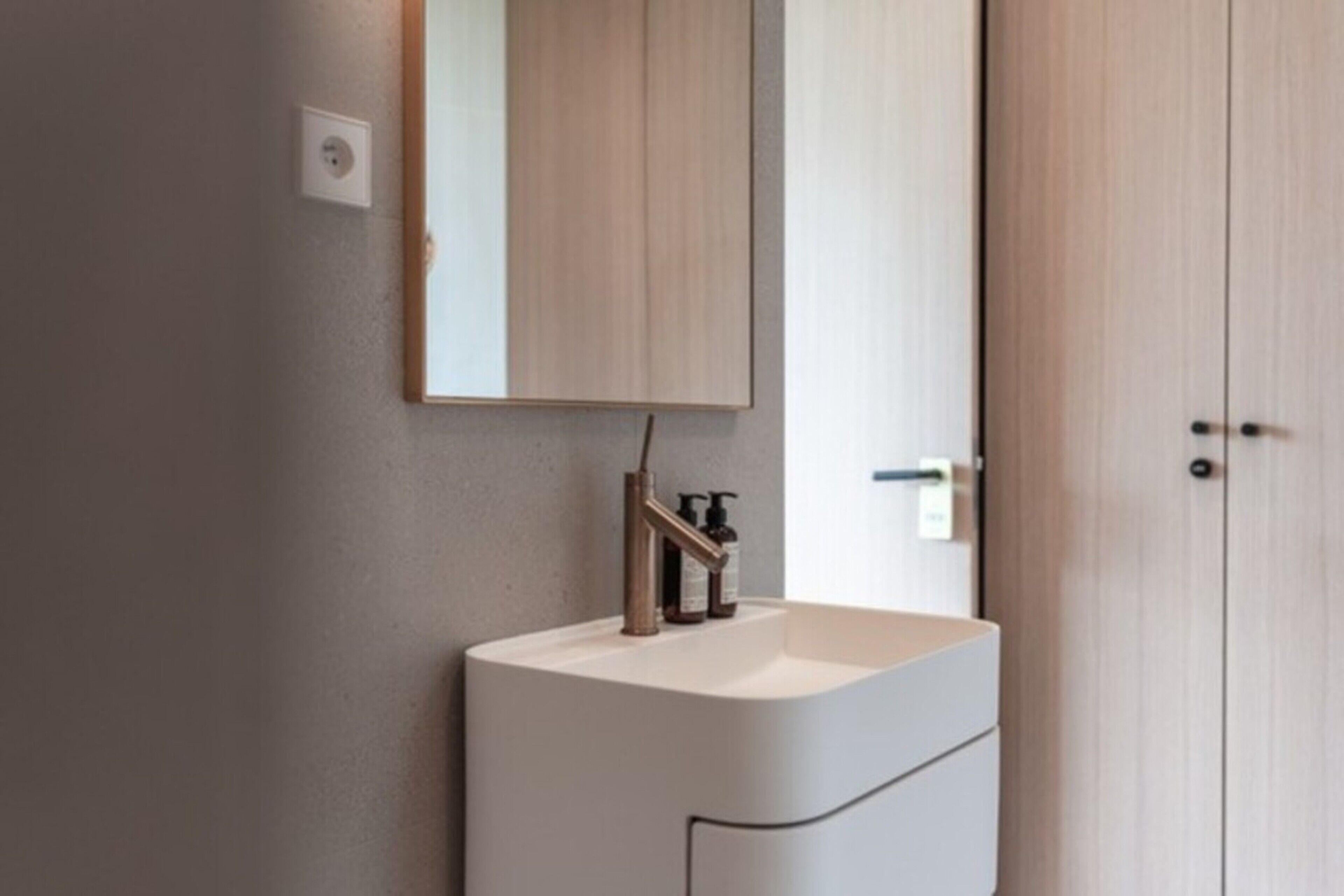 Un baño moderno con un tocador blanco, un espejo y una puerta.