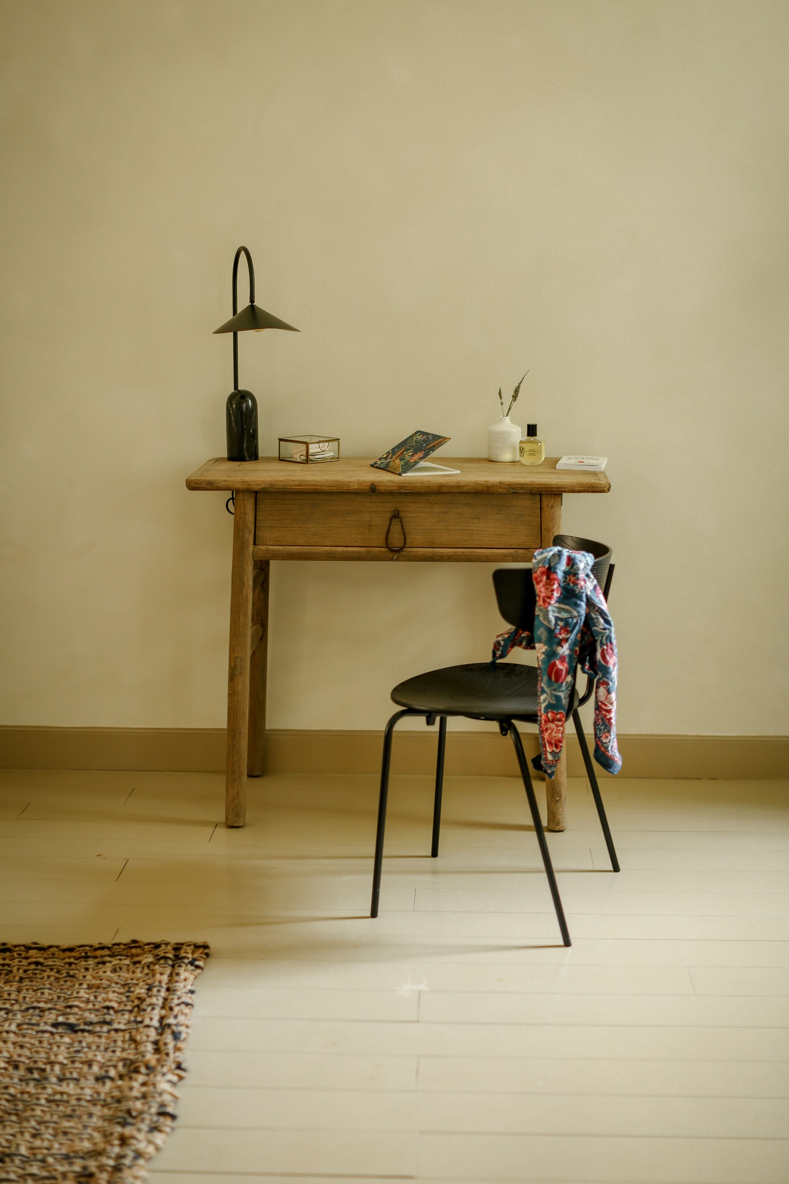 A wooden desk with a lamp, a chair, and a small table with items on it.
