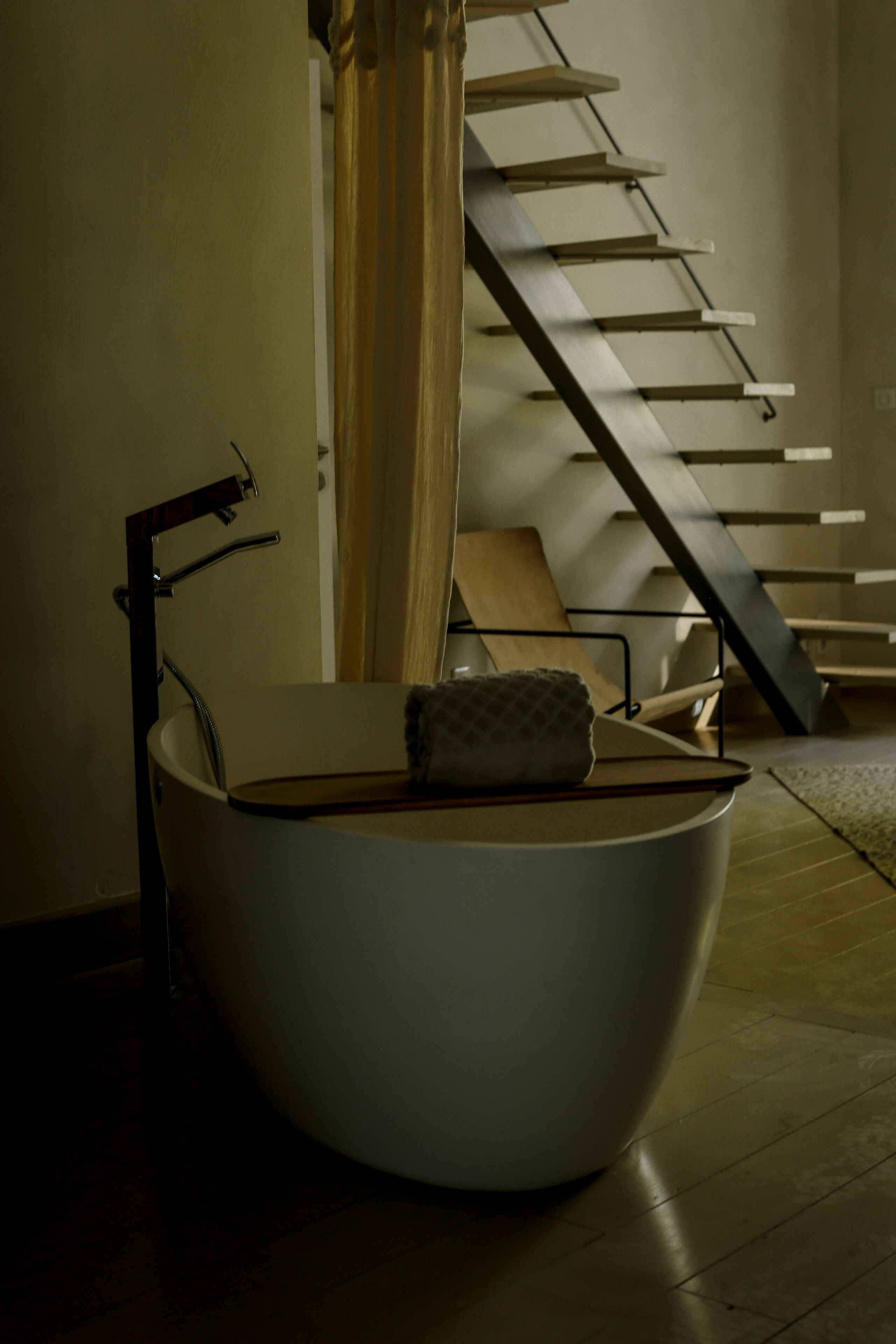 Un baño moderno con una bañera independiente, un cabezal de ducha y una escalera al fondo.
