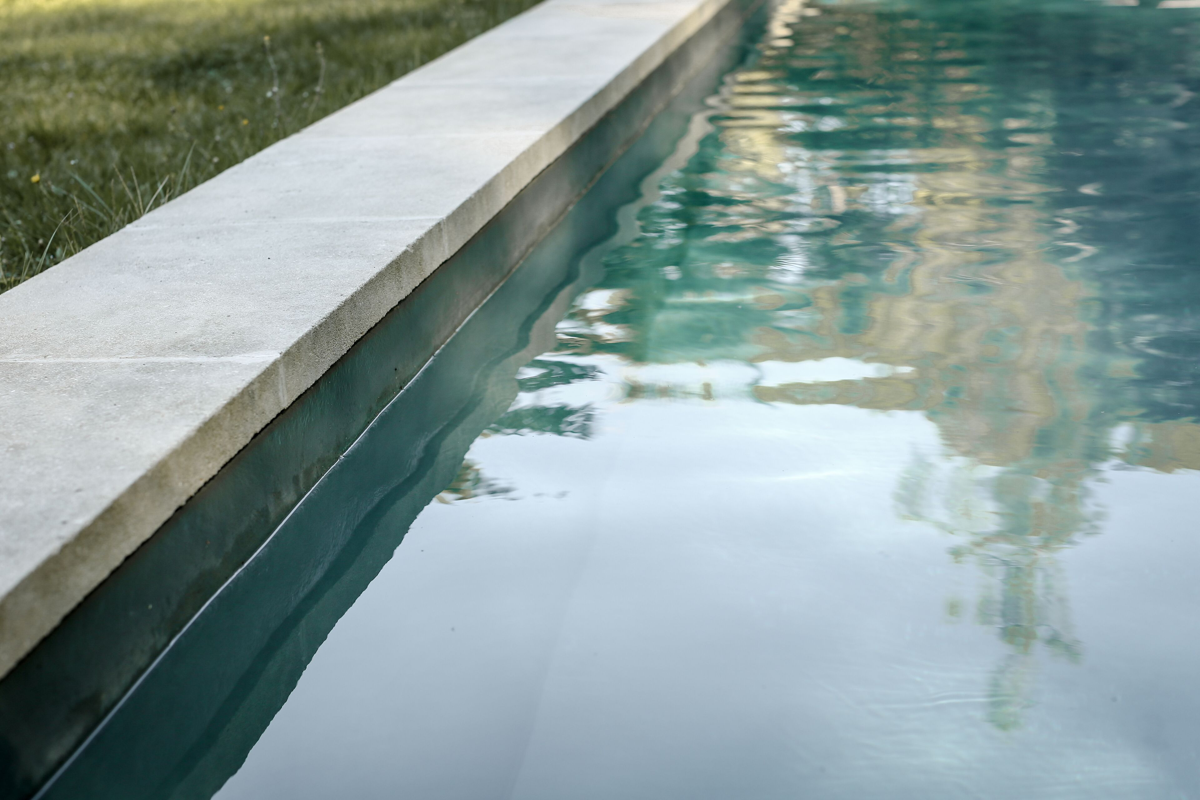 A swimming pool with a concrete edge and clear water reflecting the surroundings.