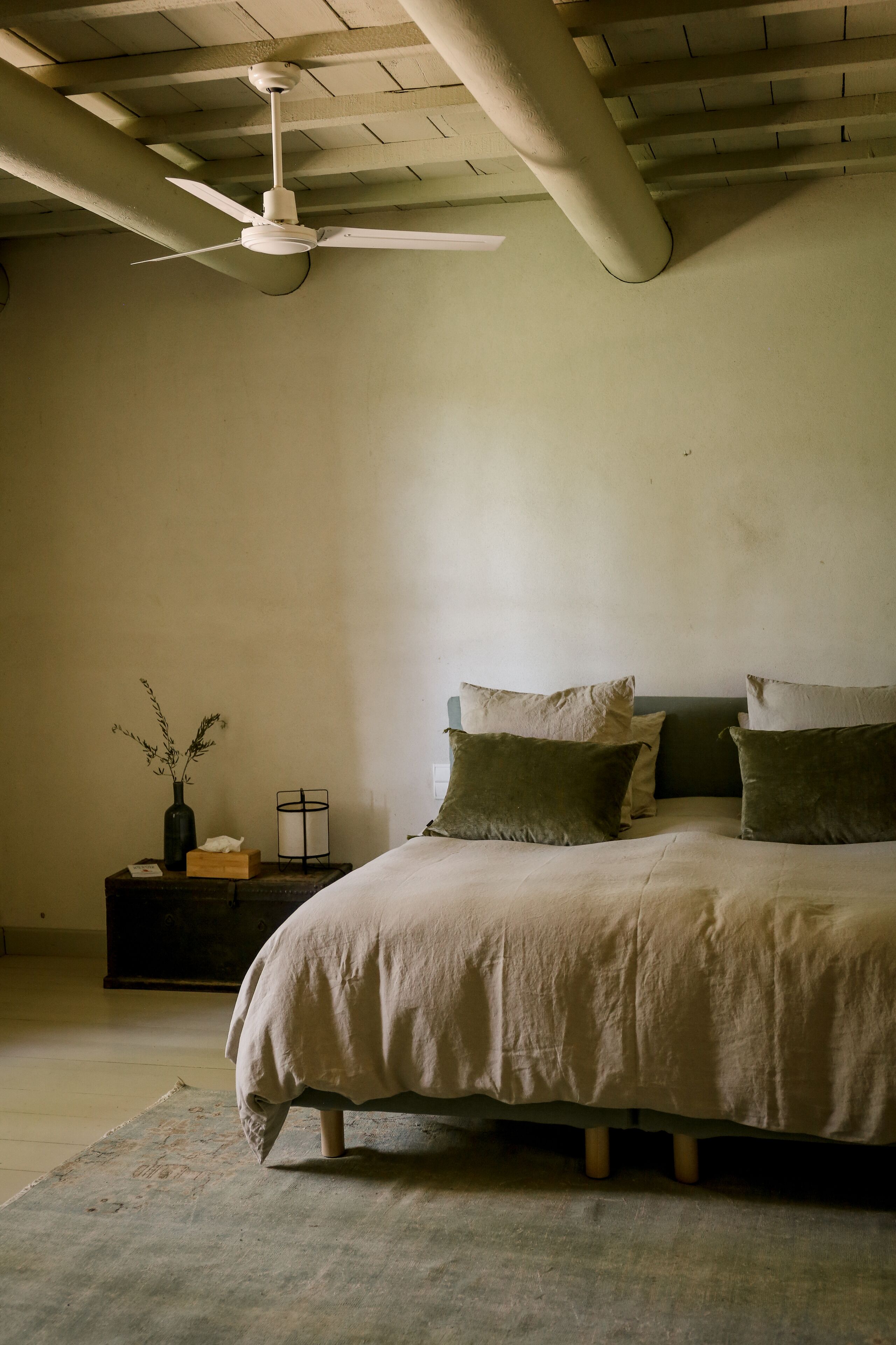 A bedroom with a bed, a nightstand, a vase, and a ceiling fan.