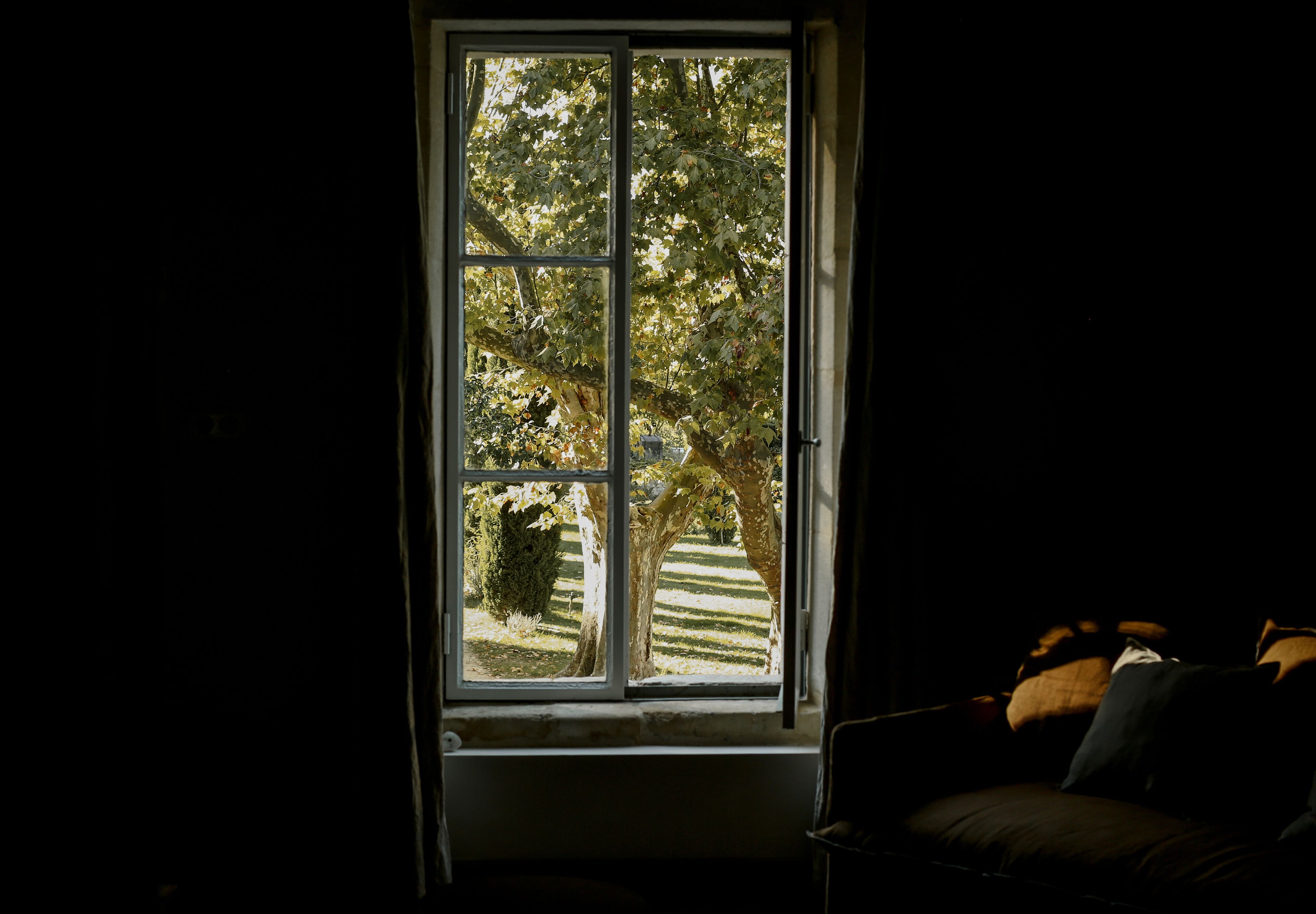 Een kamer met een groot raam, een bank en uitzicht op bomen en een gazon.