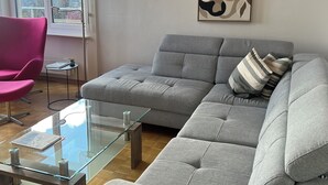 Un salon moderne avec un canapé gris, une table basse en verre, un fauteuil rose et un lampadaire.