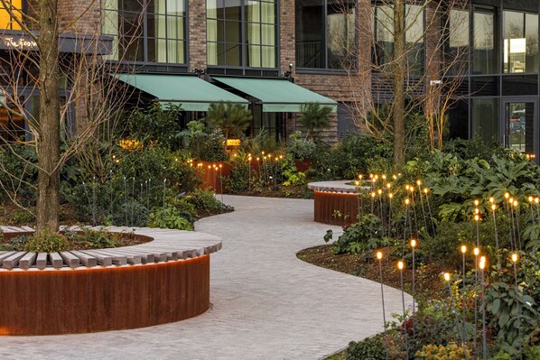 A landscaped outdoor area with a curved pathway, wooden planters, and string lights.