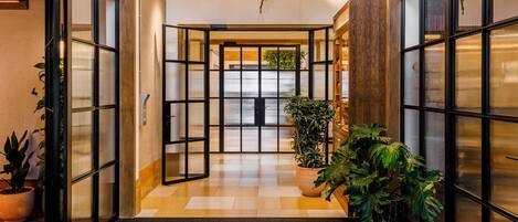 Un moderno vestíbulo de hotel con suelo de madera, amplias puertas de cristal y plantas en macetas.