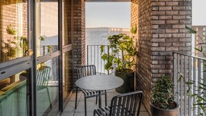 Ein Balkon mit rundem Tisch und Stühlen, Topfpflanzen und Blick auf die Stadt.