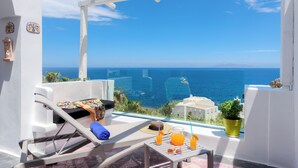A balcony with a white chair, a table with drinks, and a view of the sea. - Moschatos Beach House (Santorini)