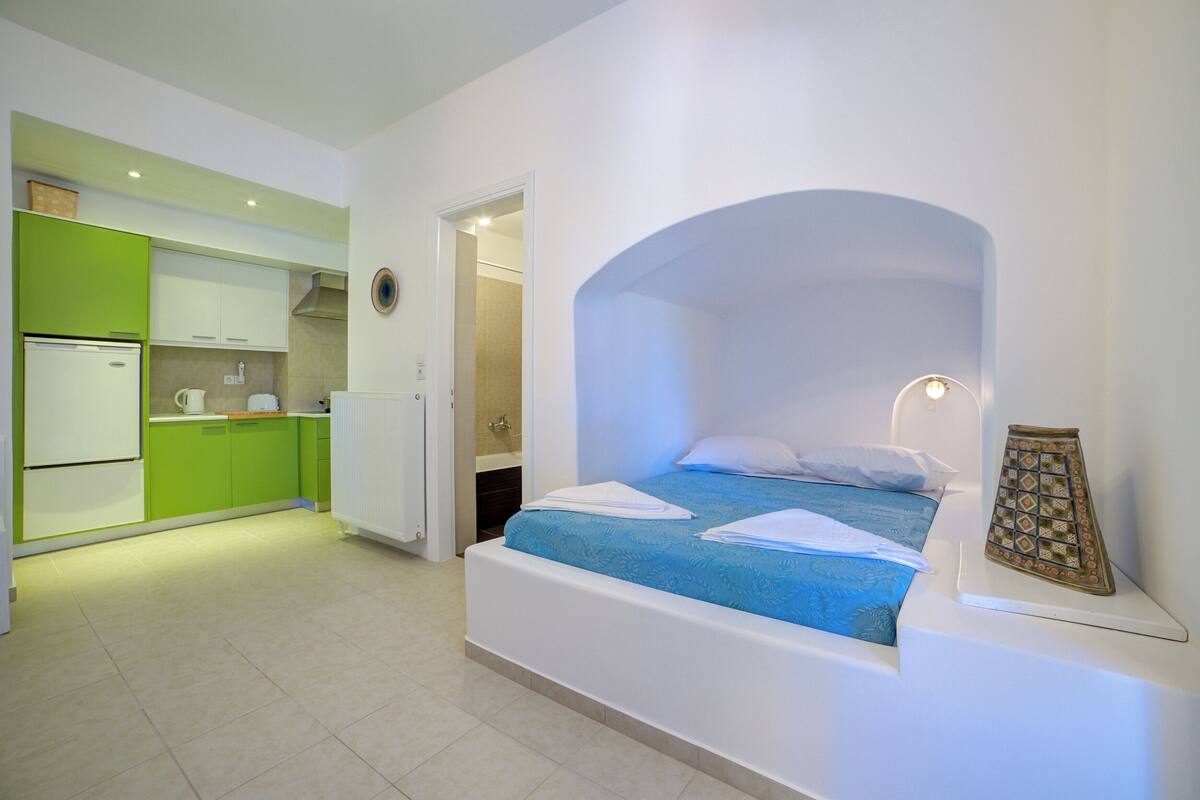 Ett modernt hotellrum med ett litet pentry, en säng med blått sänglinne och en liten prydnadsföremål på nattduksbordet.