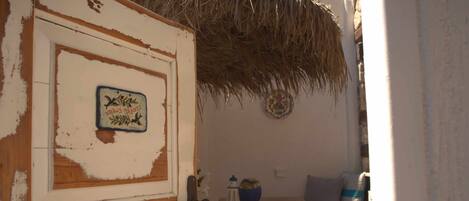 A room with a rustic door, a small table with a bowl and a candle, and a bed with a blue blanket.