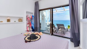A bedroom with a large bed, a view of the sea, and a balcony with a chair and table. - Moschatos Beach House (Santorini)