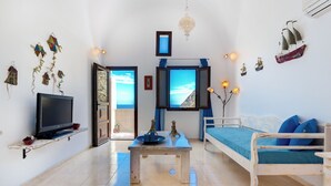 A living room with a TV, a wooden table, a sofa, and decorative items on the walls. - Moschatos Beach House (Santorini)