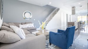 A modern living room with a grey sofa, a blue armchair, and a coffee table. A staircase is visible in the background leading to an upper level. - NEW Townhouse in Coconut Grove (Coconut Grove)